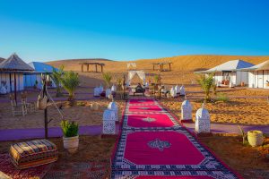 Scenic road to Merzouga with desert dunes and camel caravan in the background – journey from Marrakech, Fes, or Casablanca.