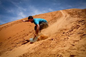 Adventurer sandboarding down the golden dunes of Merzouga in the Sahara Desert, capturing the thrill of the desert adventure.